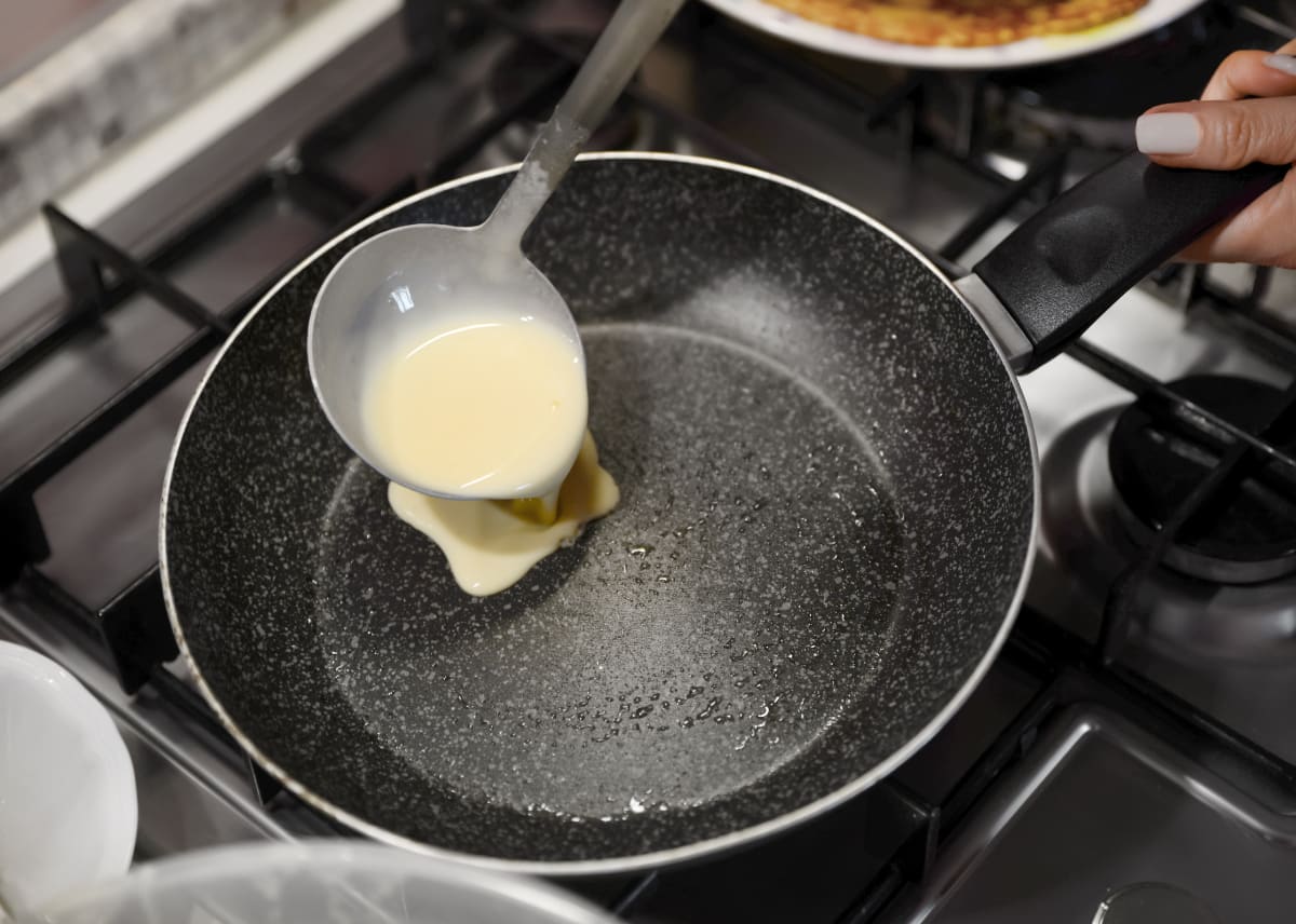 Pouring pancake batter into a pan with a spoon